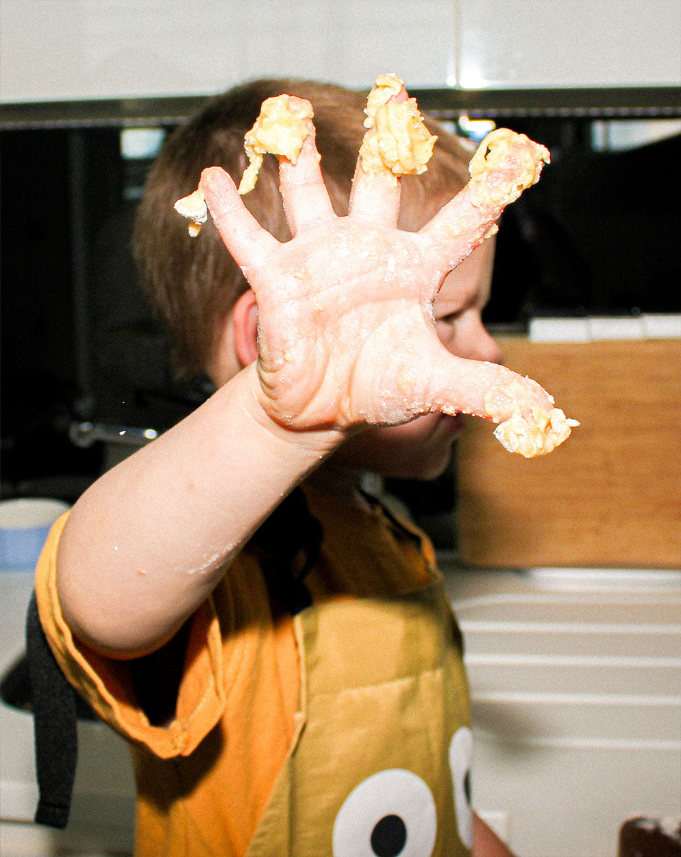 A close-up of a child’s hand covered in dough, held up to the camera while wearing the Kindy™ apron. Captures the sensory experience of baking and the importance of mess-friendly, protective gear for toddler independence.