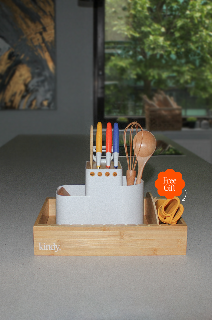 The Kindy™ Starter Bundle showcased on a kitchen counter: includes the white KindyCook tool holder with safety knives, bamboo whisk and spoon, and the bamboo KindyFlex adjustable organiser for plates and cups. A complete Montessori kitchen starter kit for toddlers.