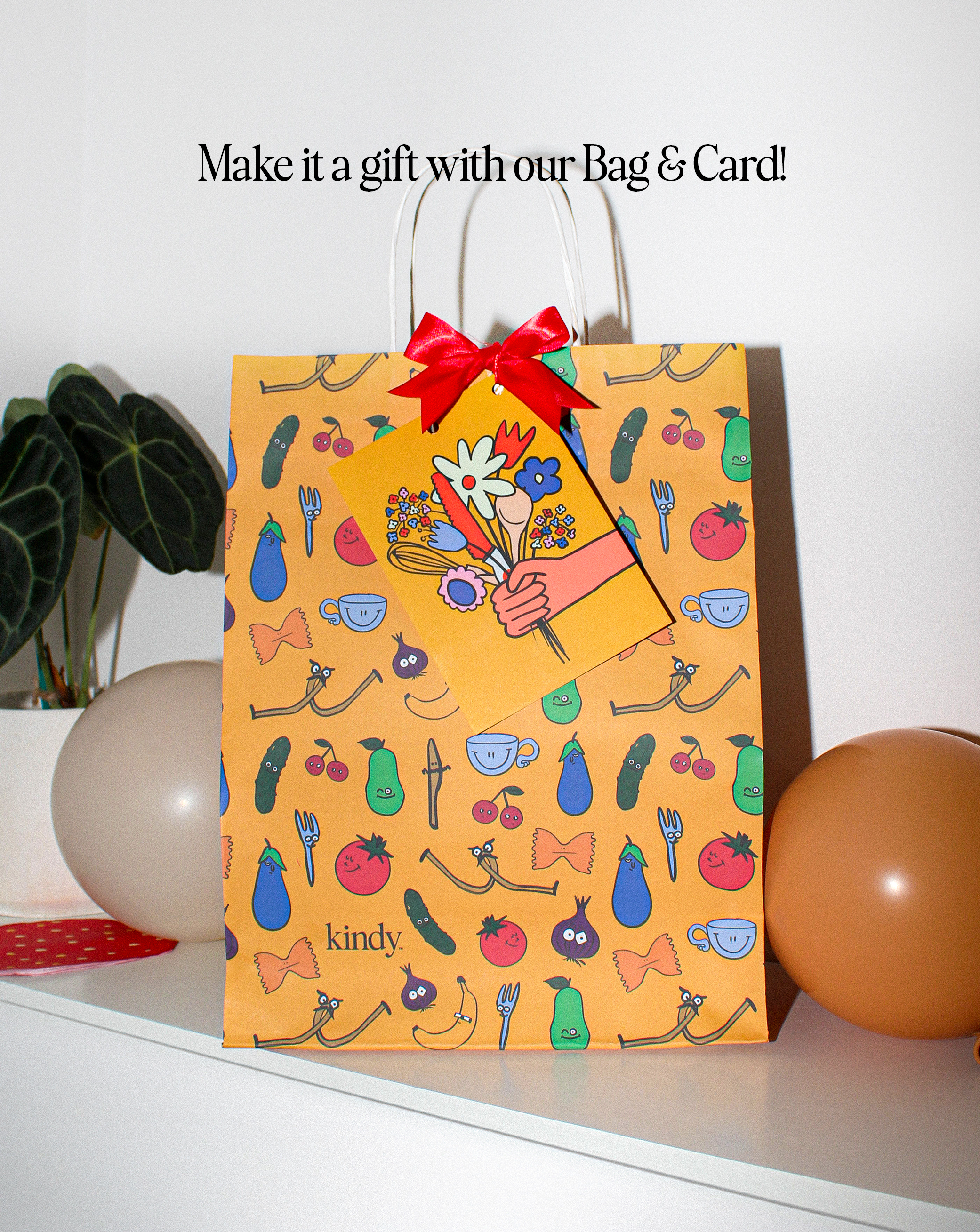 A festive Kindy™ branded paper gift bag with a red bow and illustrated vegetable pattern. A beautiful 'ready-to-gift' option for non-chocolate Easter gifts or toddler birthday surprises.